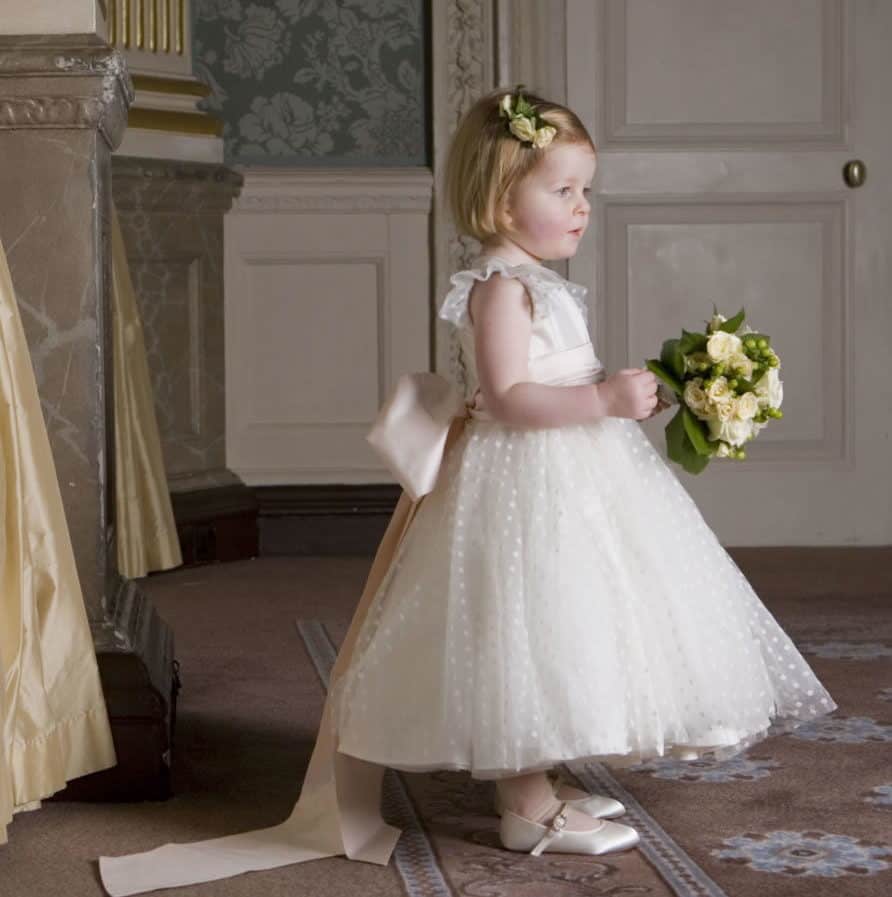 flower girl with classic royal style dress with a pink ribbon by Nicki Macfarlane