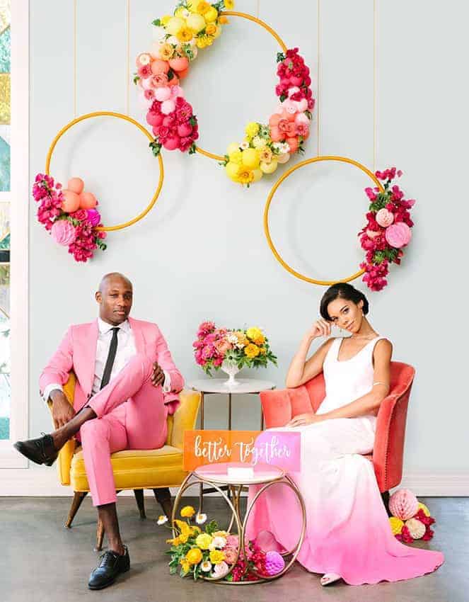 groom with pink suit and the bride with a white pink wedding dress, wedding colour decoration with hanging circles with colourful balloons and flowers