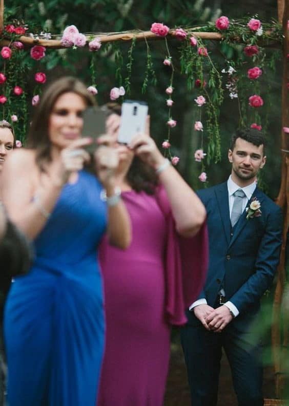during the wedding ceremony the groom waiting for the bride, and two guests trying to photograph the bride