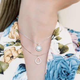 Μια γυναίκα φοράει 2 μενταγιόν, ενά ασημένιο και ένα χρωματιστό, από το Yiotis Jewellery.